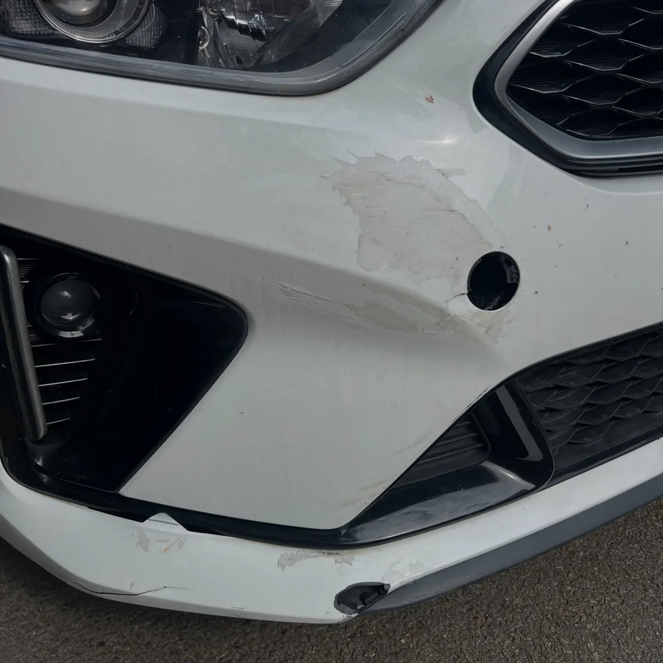 Scuffed white Kia front bumper beside the fog light